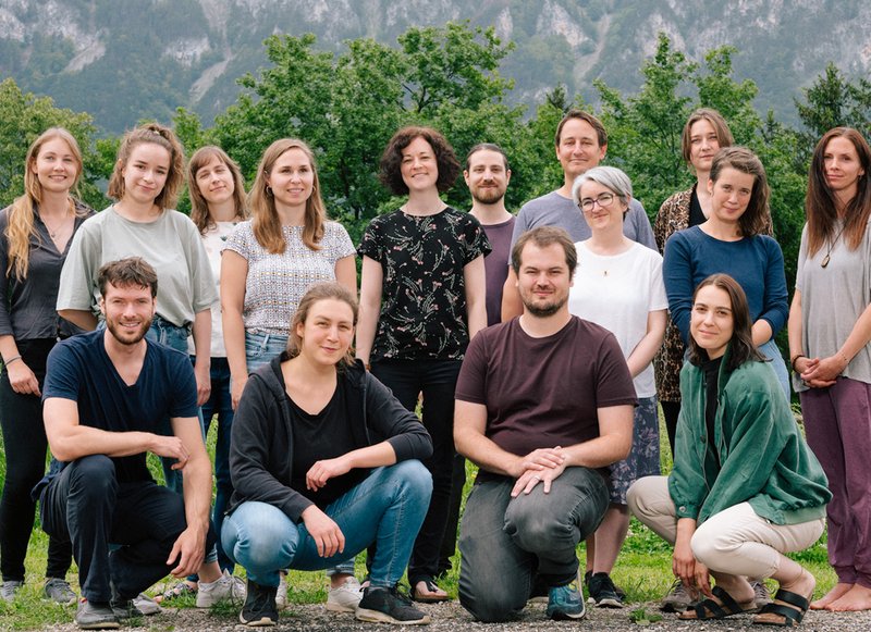 Team Mitglieder aufgereiht für ein Gruppenfoto, dahinter sind Bäume und Berge zu sehen