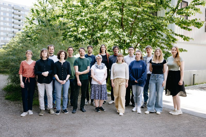 Team Mitglieder aufgereiht für ein Gruppenfoto, dahinter sind Bäume und Berge zu sehen