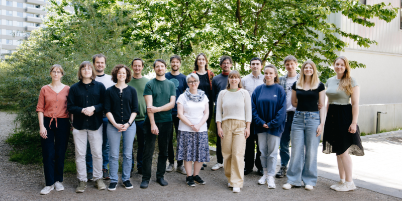 Team Mitglieder aufgereiht für ein Gruppenfoto, dahinter sind Bäume und Berge zu sehen