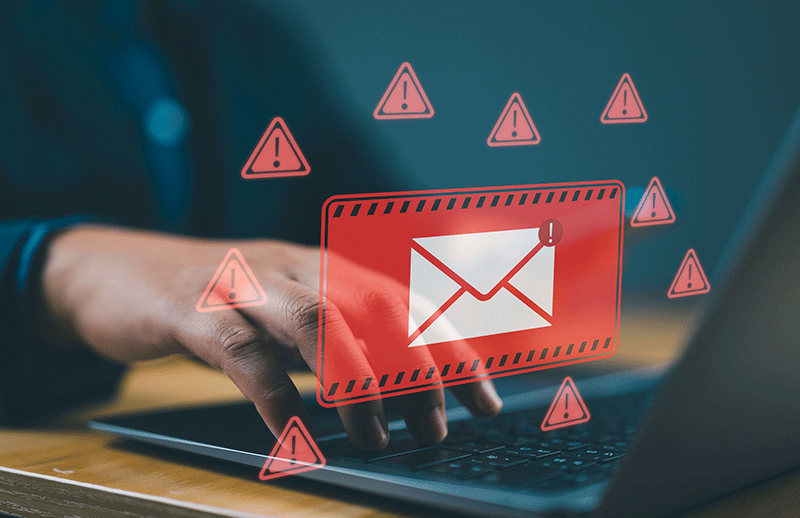 A person typing on a laptop with a red warning graphic showing an email envelope and multiple alert symbols, representing spam or phishing threats.